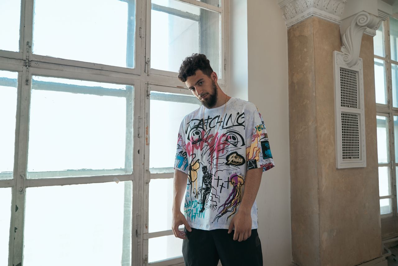 About Man in a graffiti t-shirt posing stylishly indoors with natural window light.