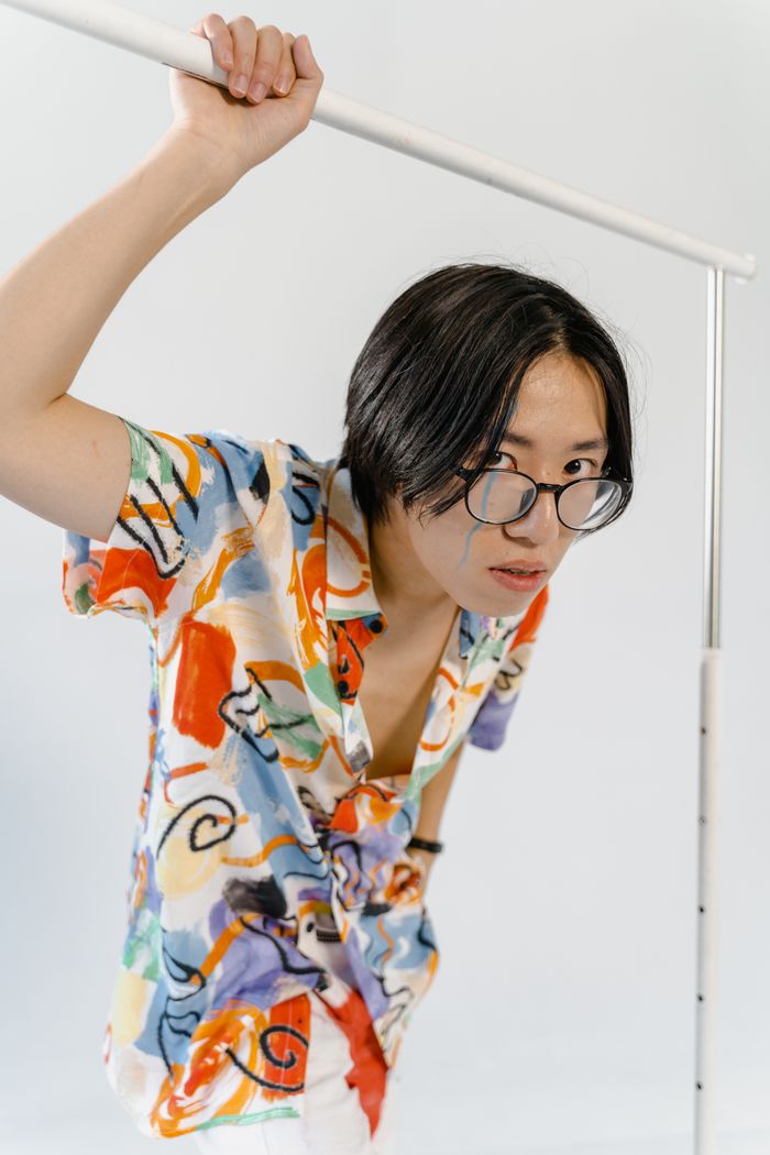 Services Asian man wearing glasses, posing with a colorful abstract shirt, exuding modern style and fashion.