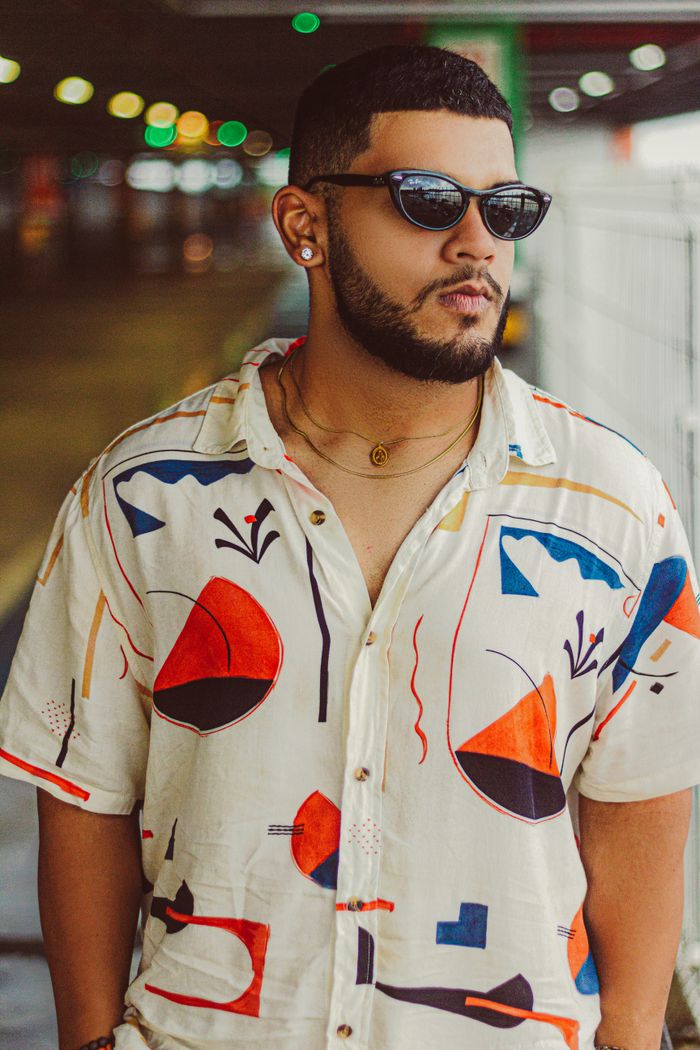 Services Portrait of a fashionable man with sunglasses, wearing an abstract-designed shirt outdoors.